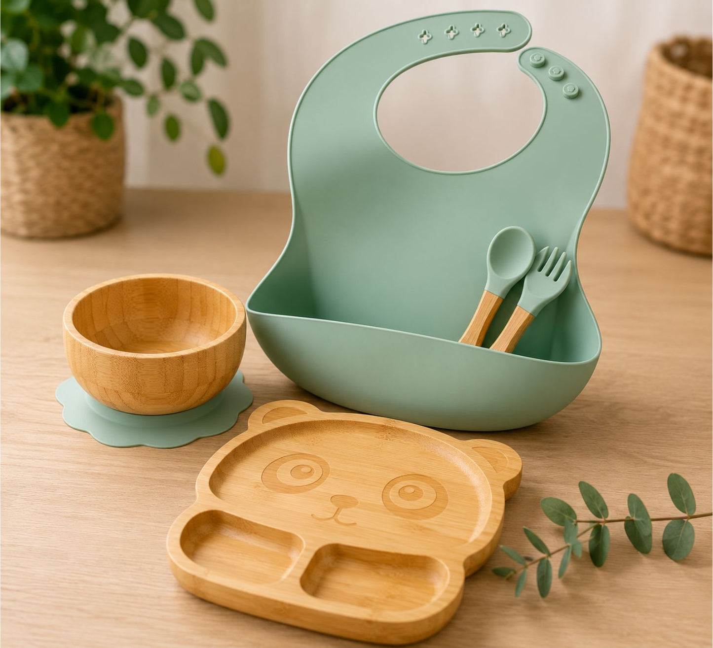 Children's dining set with green bib, eco-friendly bamboo plate, bowl, and utensils on a wooden surface.