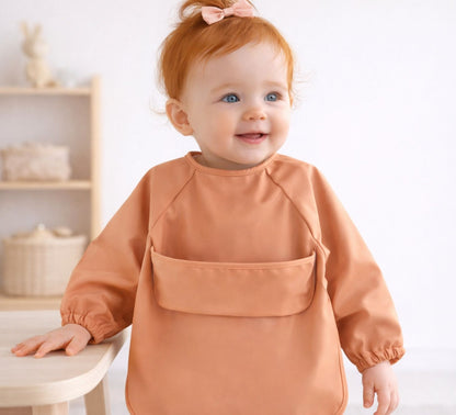 baby girl wearing an orange/caramel feeding smock long sleeves