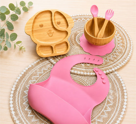 Organic bamboo dog-shaped baby feeding set with eco-friendly silicone bib, suction bowl, and wooden spoon and fork in pink colour.