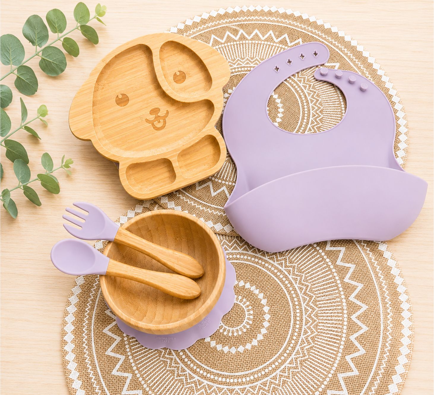Organic bamboo dog-shaped baby feeding set with eco-friendly silicone bib, suction bowl, and wooden spoon and fork in purple colour.